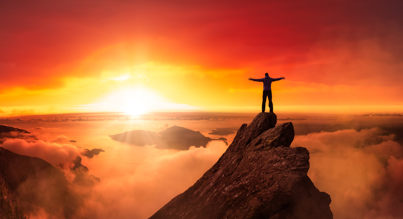Man Standing on Top of a Mountain Against the Sunset